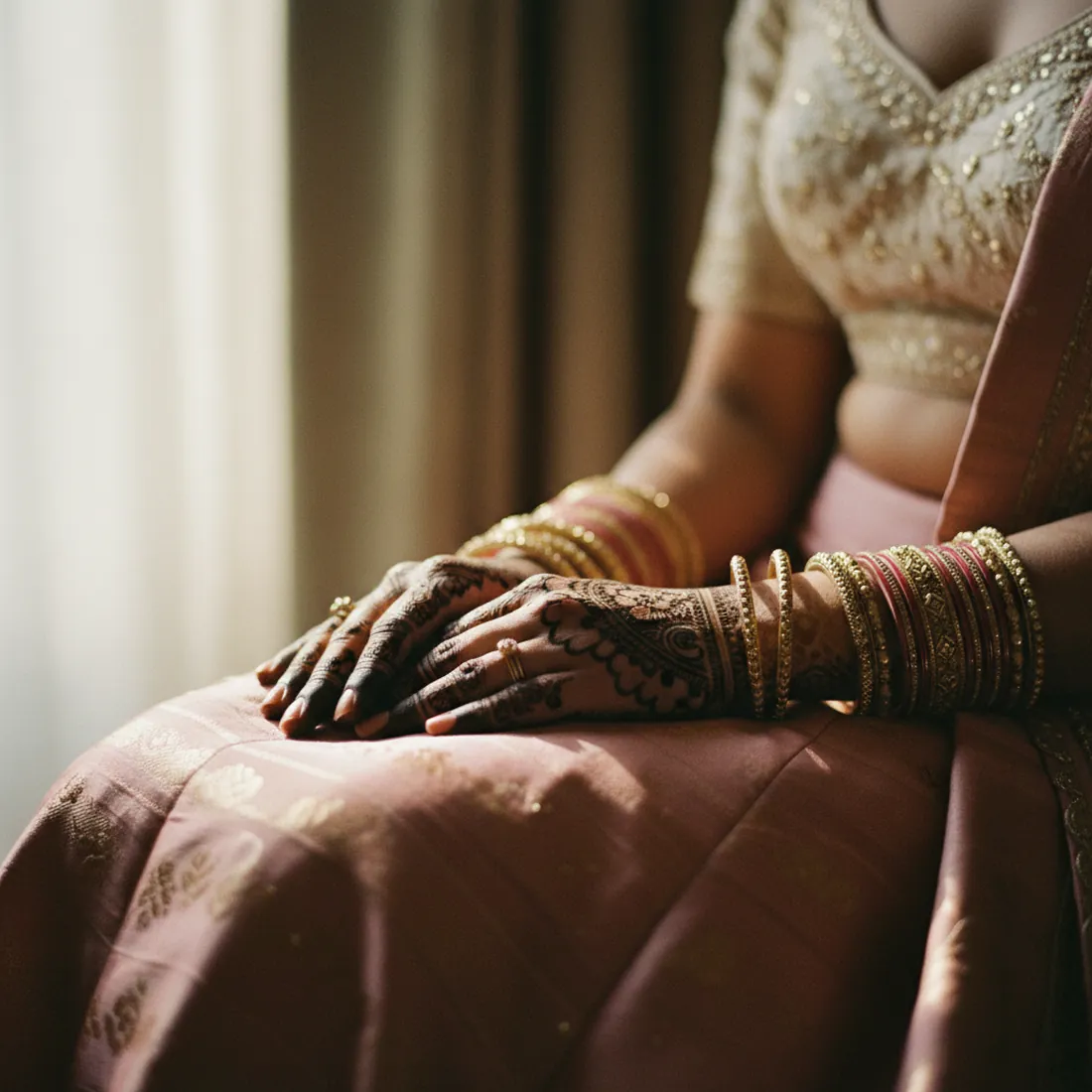 A bride's hands in her lap with fresh mehndi on the palms and gold bangles at the wrist